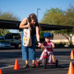 A mother assists her child in riding a tricycle on an obstacle course at Maricopa Police Department's inaugural bicycle rodeo on April 24, 2026. [Monica D. Spencer]