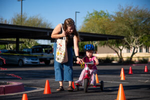 A mother assists her child in riding a tricycle on an obstacle course at Maricopa Police Department's inaugural bicycle rodeo on April 24, 2026. [Monica D. Spencer]