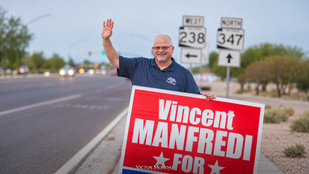Vincent Manfredi waves while holding a campaign sign near SR 238 and SR 347 signs in Maricopa.