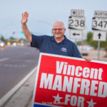 Vincent Manfredi waves while holding a campaign sign near SR 238 and SR 347 signs in Maricopa.