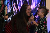 Natalie Davis and son, Elijah, share a moment while onstage at the Maricopa's Got Talent auditions Saturday night with husband and father, Paul Davis, playing in the background. [Photo by Karen Bartunek on Aug. 29, 2026.]